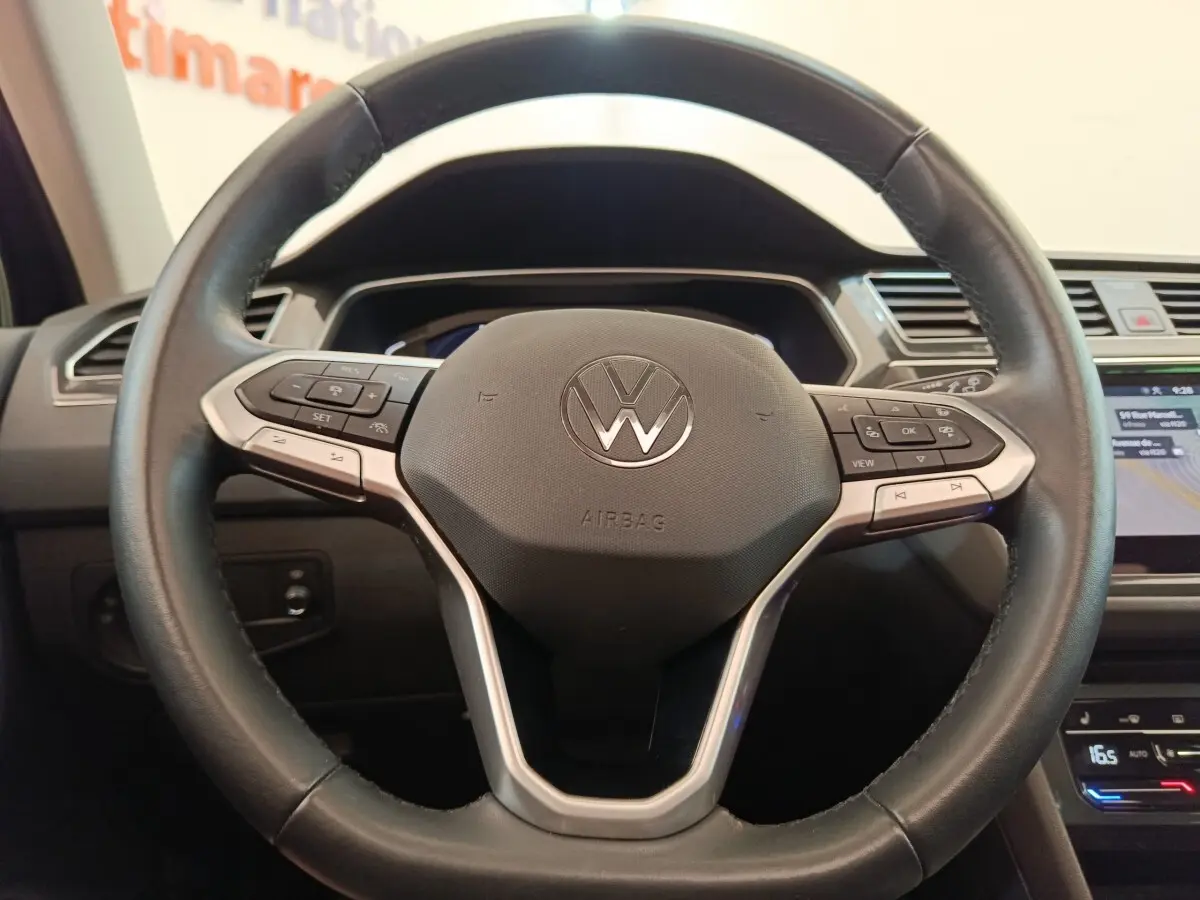 Gros plan sur le volant cuir multifonctions du Volkswagen Tiguan 1.4 eHybrid noir, avec commandes intégrées.