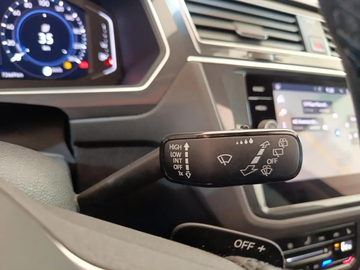 Gros plan sur la commande des essuie-glaces dans l’habitacle du Volkswagen Tiguan noir, avec tableau de bord numérique en arrière-plan.