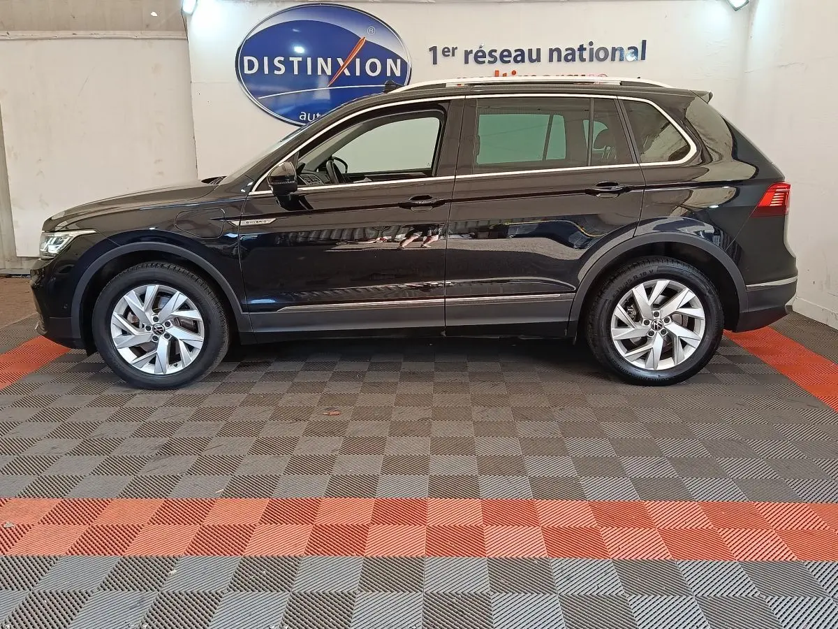 Vue de profil côté gauche d'un Volkswagen Tiguan noir 1.4 eHybrid 245 DSG6 Elegance Exclusive dans un showroom.