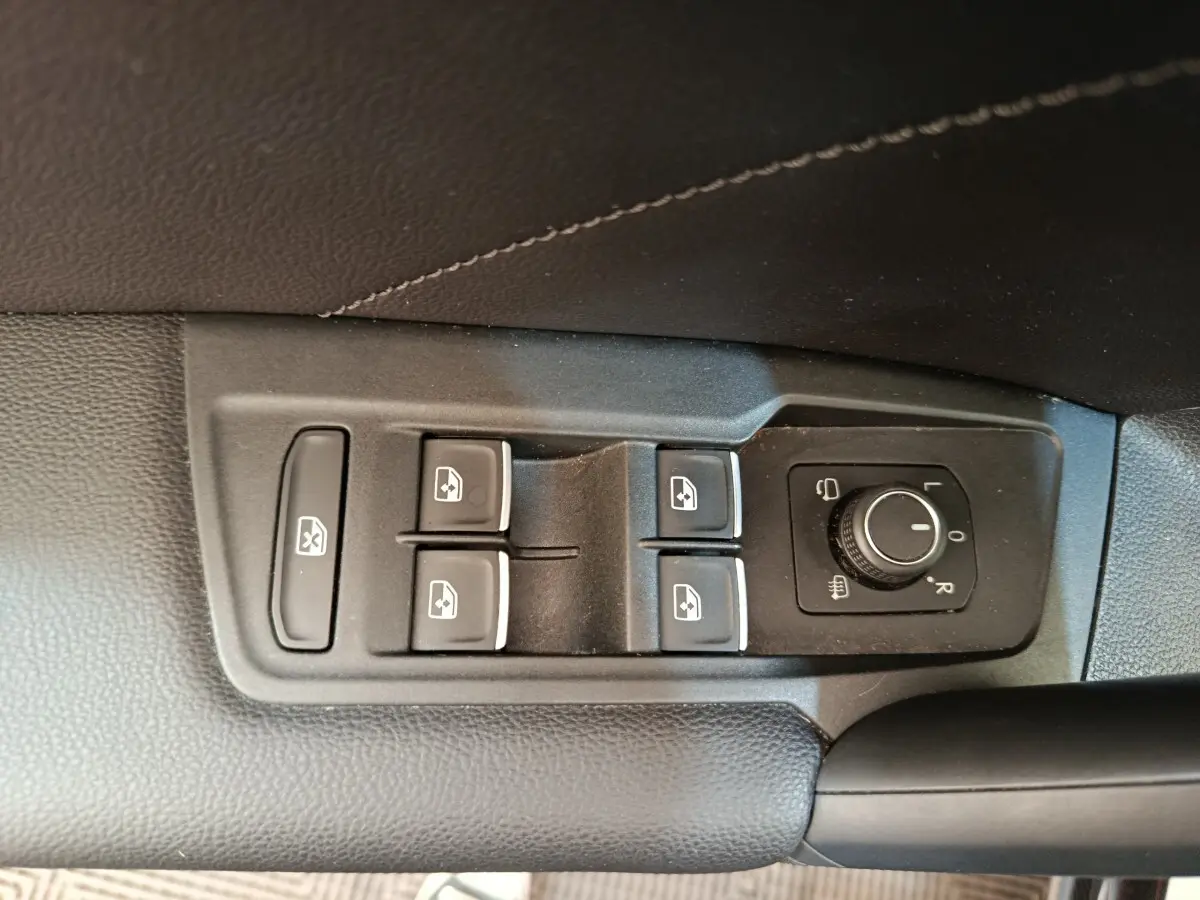 Gros plan sur les commandes de lève-vitres et réglage des rétroviseurs côté conducteur d’un Volkswagen Tiguan noir.