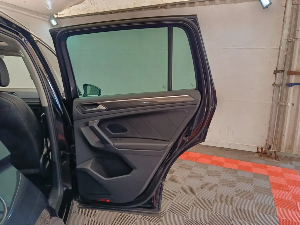 Vue intérieure côté arrière gauche du Volkswagen Tiguan noir 2022, porte ouverte avec garniture et poignée visibles.