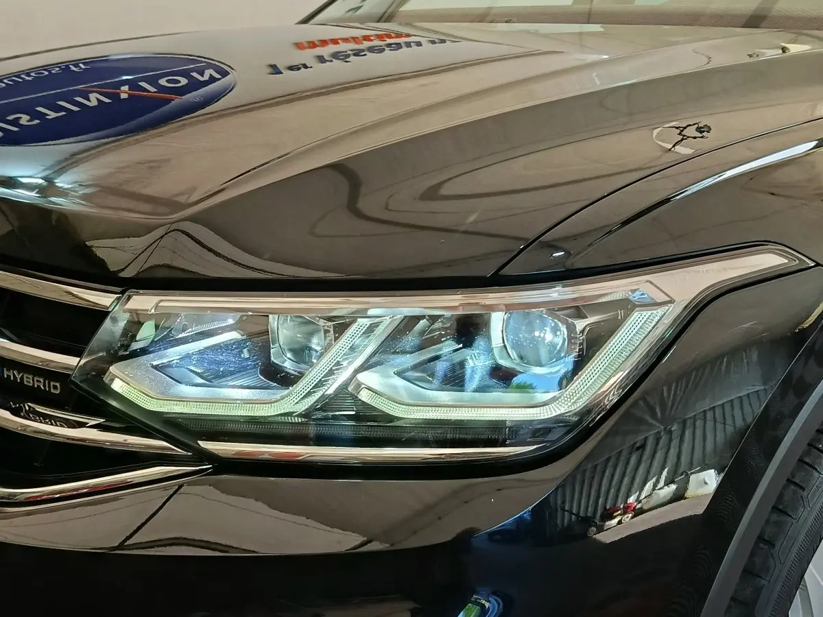 Gros plan sur le phare avant droit LED du Volkswagen Tiguan noir, mettant en valeur les détails lumineux et la calandre hybride.