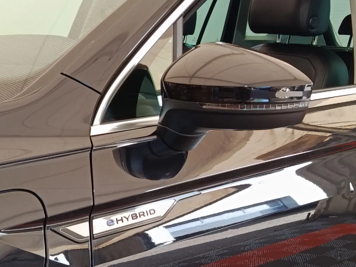 Gros plan sur le rétroviseur droit et l’inscription eHybrid d’un Volkswagen Tiguan noir brillant.
