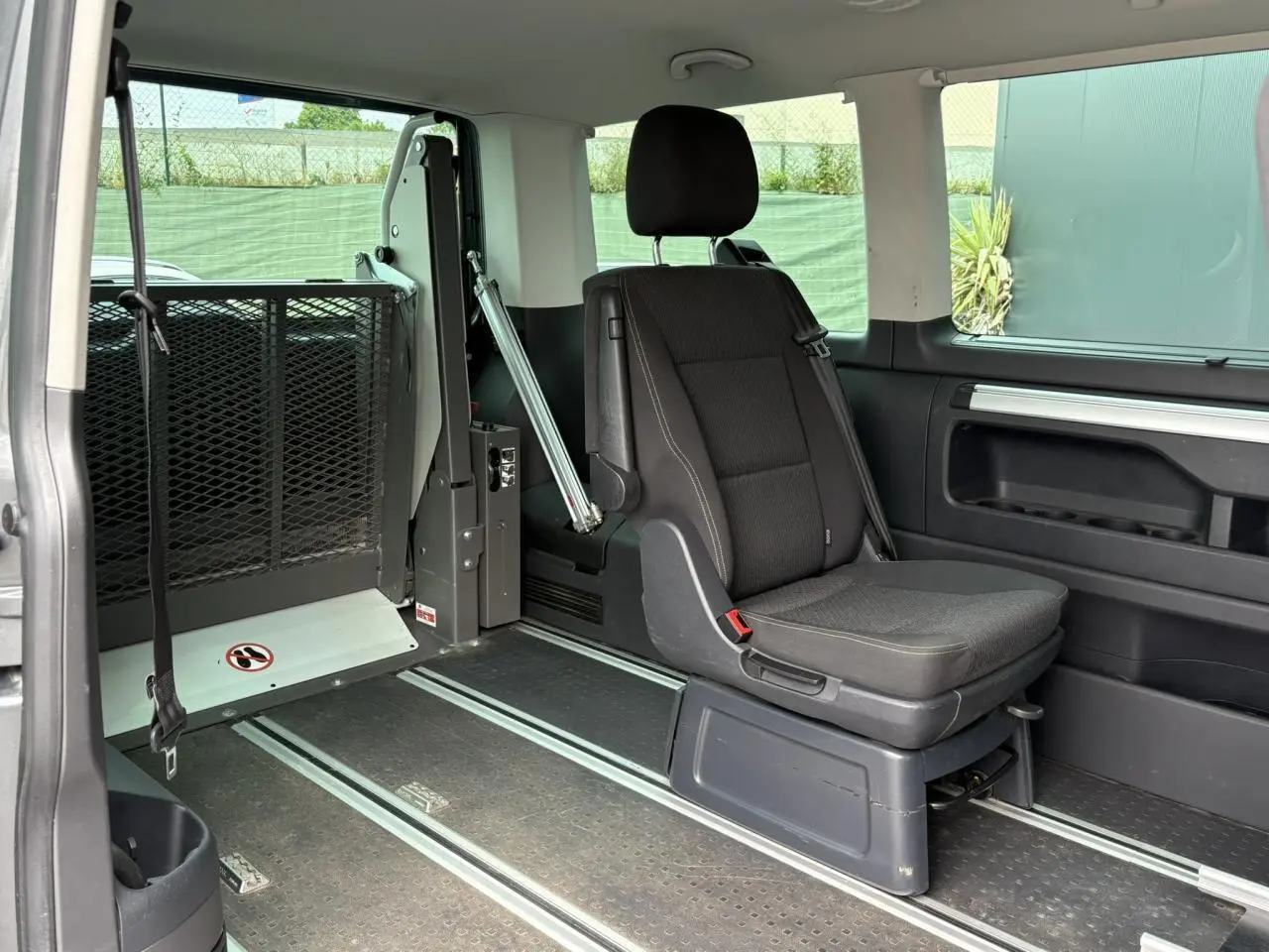 Siège passager noir et aménagement TPMR visibles à l'intérieur d'un Volkswagen Multivan gris Indium, vue latérale droite.