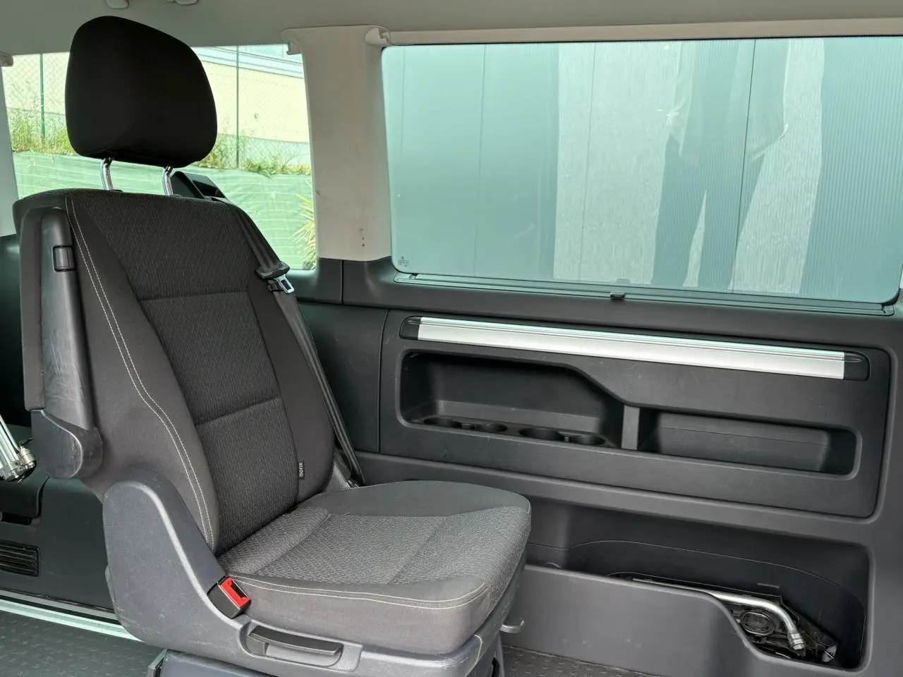 Siège passager arrière noir du Volkswagen Multivan T6 2019 avec porte coulissante droite et fenêtre teintée.