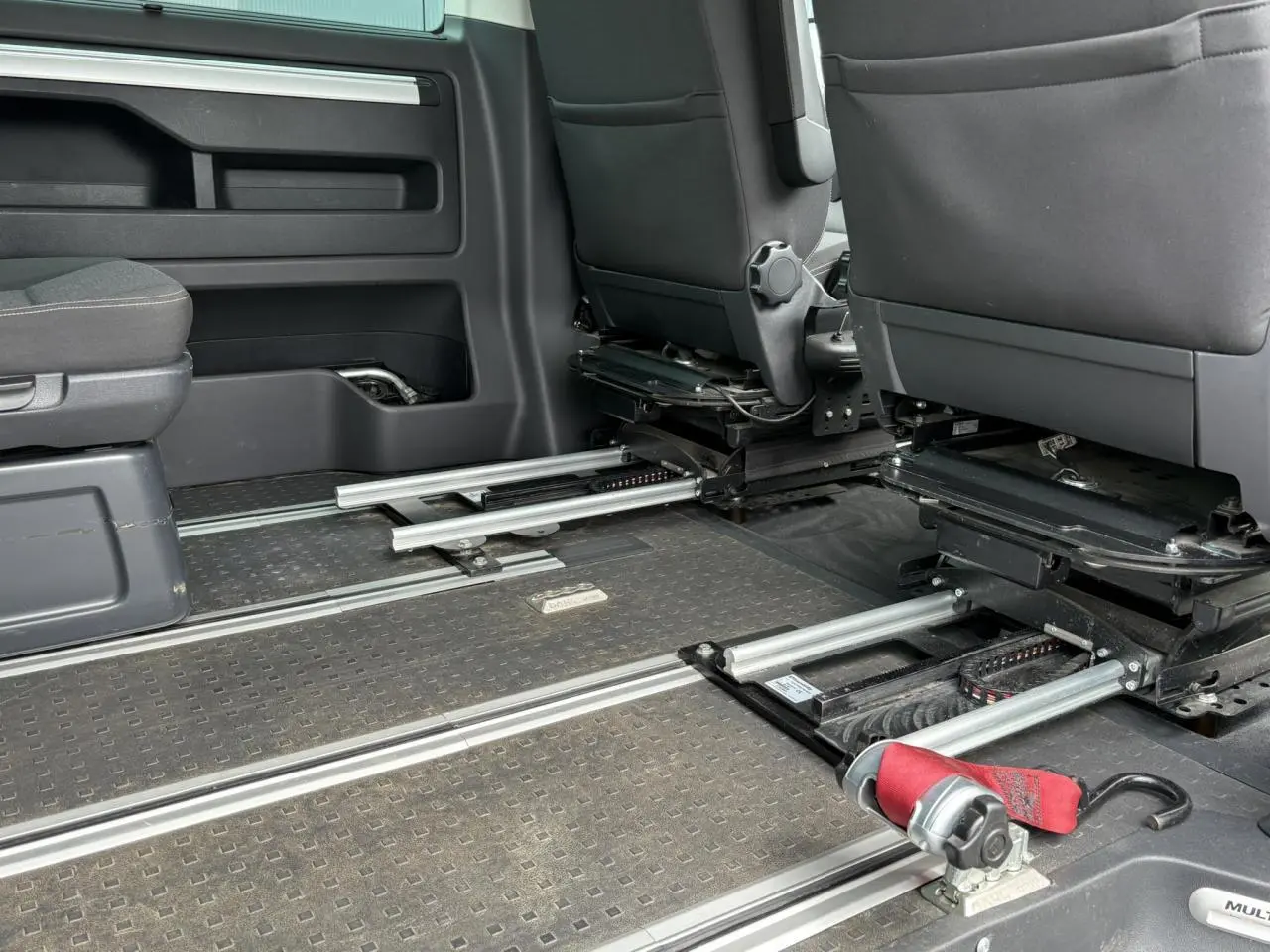 Vue intérieure du Volkswagen Multivan T6 TPMR montrant les rails au sol et les sièges avant gris foncé.