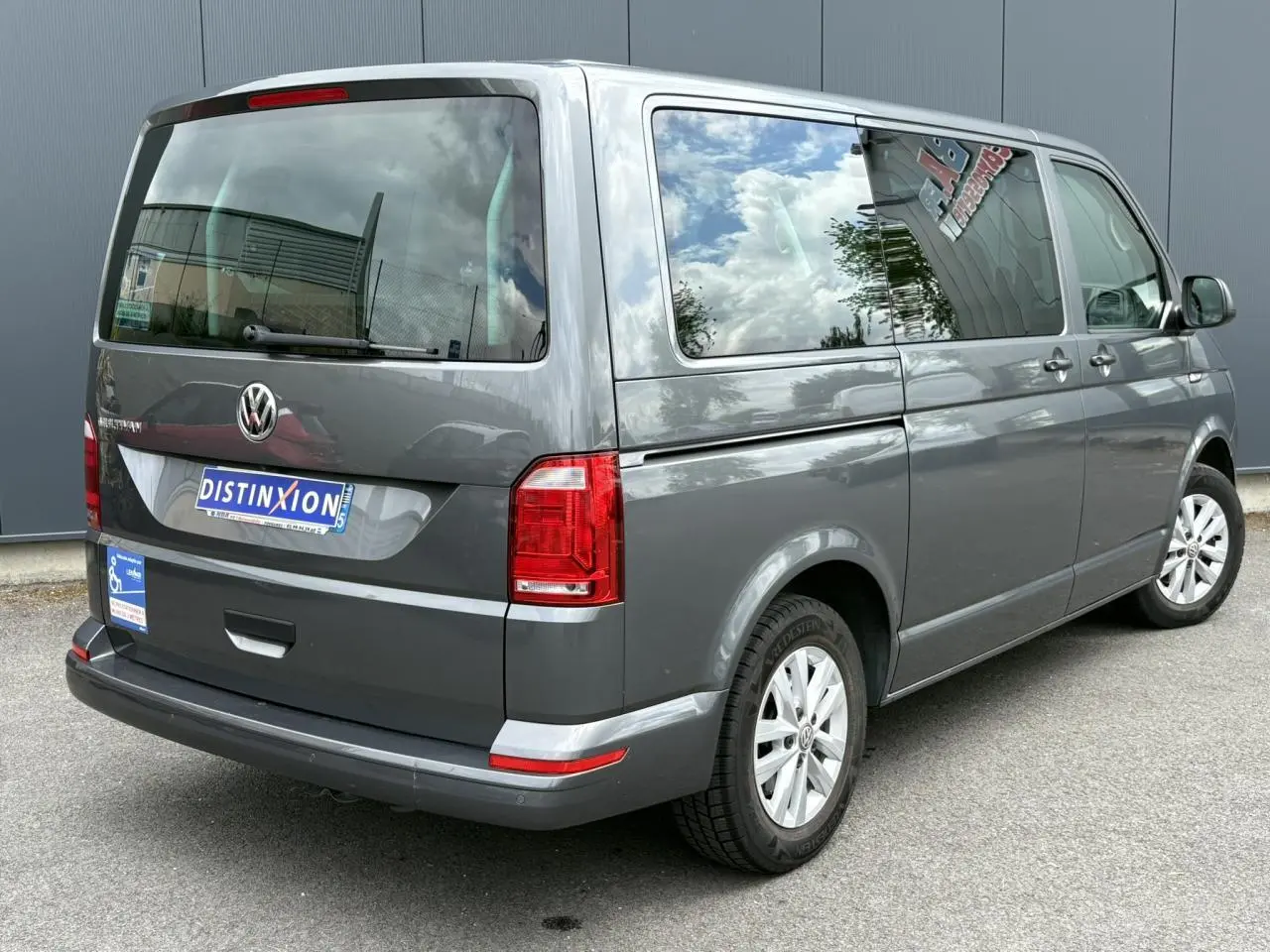 Vue 3/4 arrière droite d'un Volkswagen Multivan T6 gris Indium avec vitres teintées et jantes alliage léger.