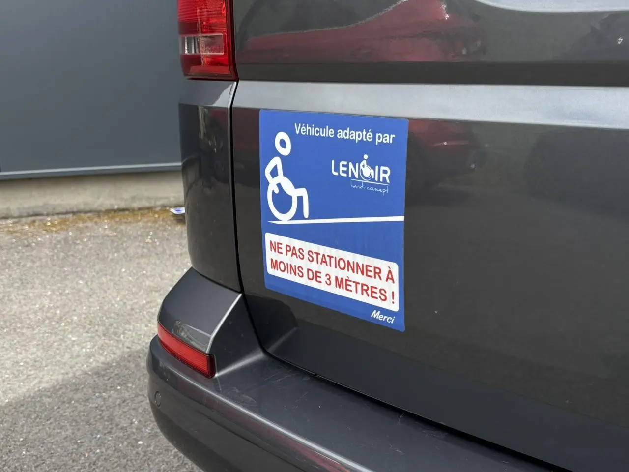 Vue arrière gauche du Volkswagen Multivan gris Indium avec autocollant handicap et message de stationnement interdit.