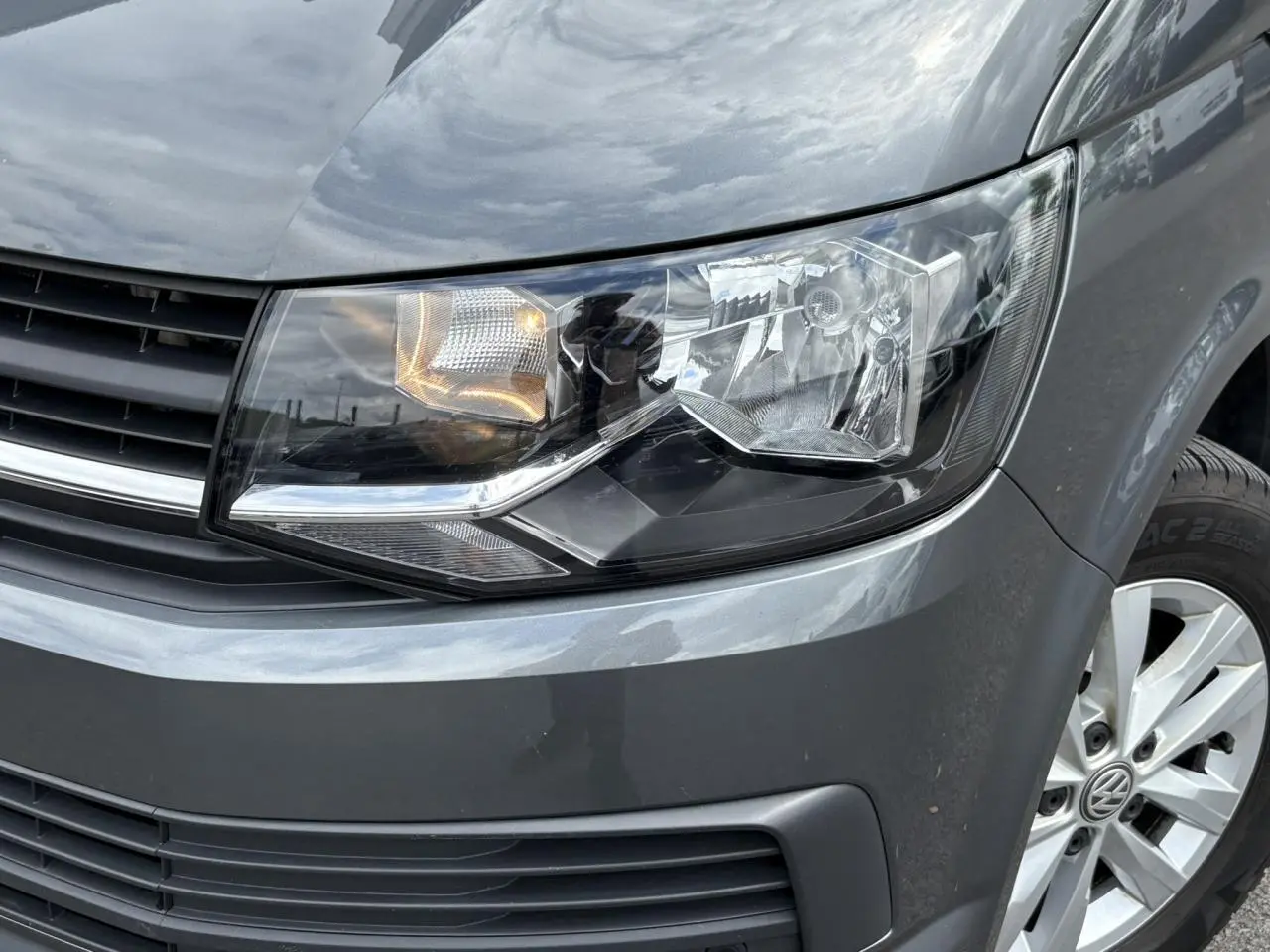 Gros plan sur le phare avant droit et la calandre d'un Volkswagen Multivan gris Indium avec jante alliage visible.