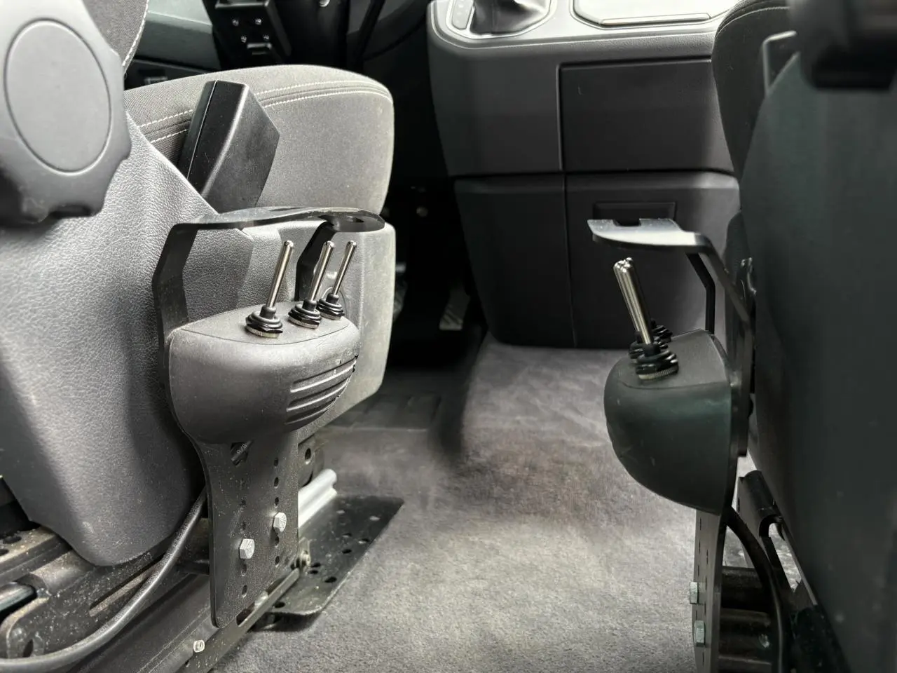 Gros plan sur les commandes manuelles d'accessibilité entre les sièges avant du Volkswagen Multivan T6 gris Indium.