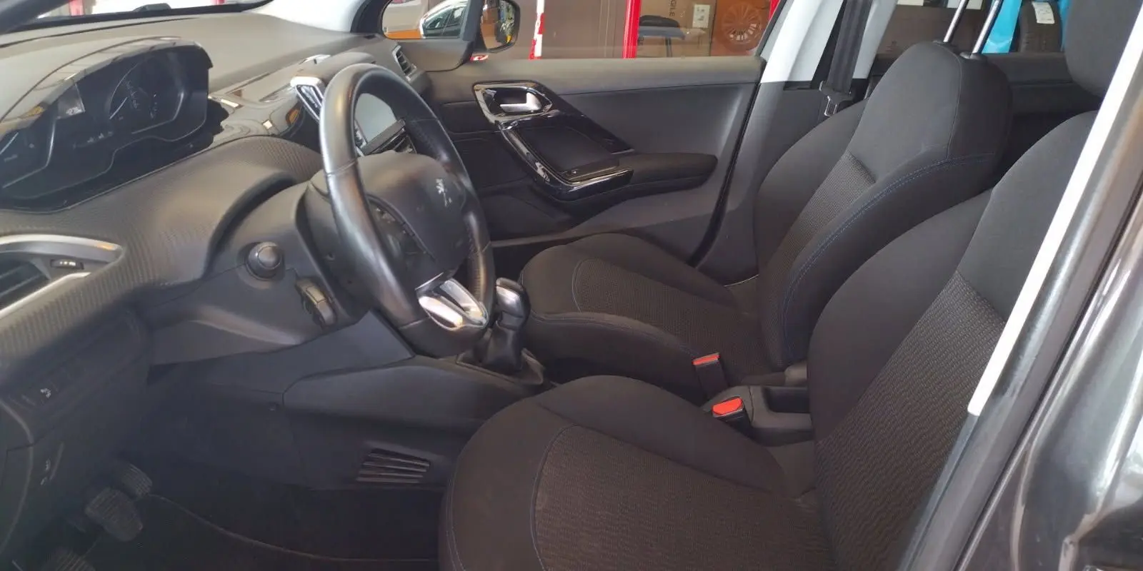 Intérieur avant gauche de la Peugeot 208 1.6l HDi 75 ch 2023 avec sièges noirs et volant cuir.