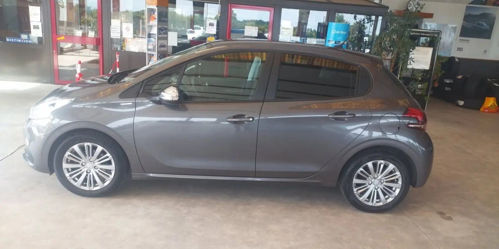 Profil côté gauche d'une Peugeot 208 gris métal 2023, compacte et élégante, en intérieur de showroom lumineux.