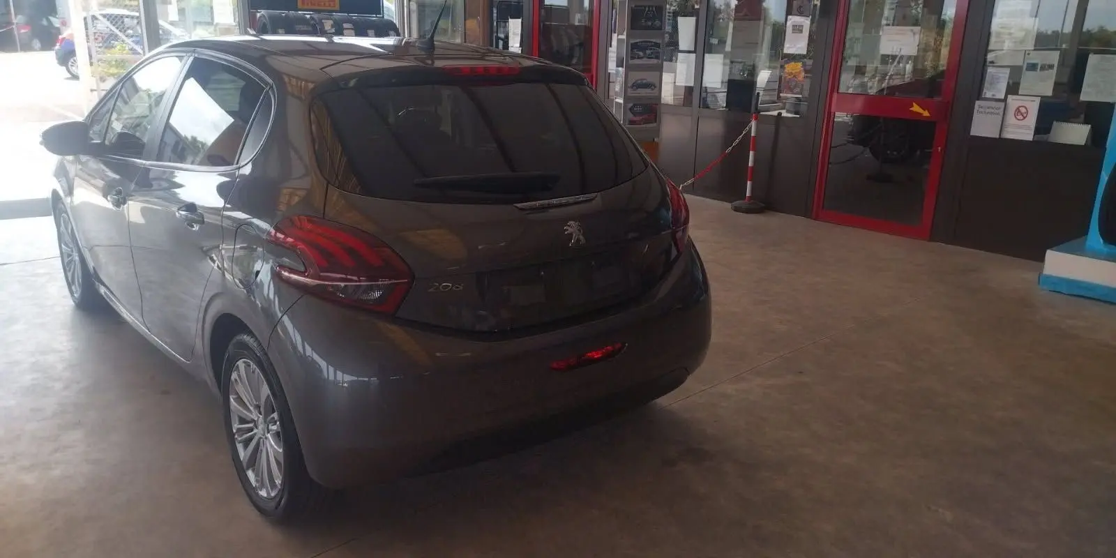 Peugeot 208 gris métal vue 3/4 arrière droit dans un showroom, avec feux arrière distinctifs et jantes alliage.