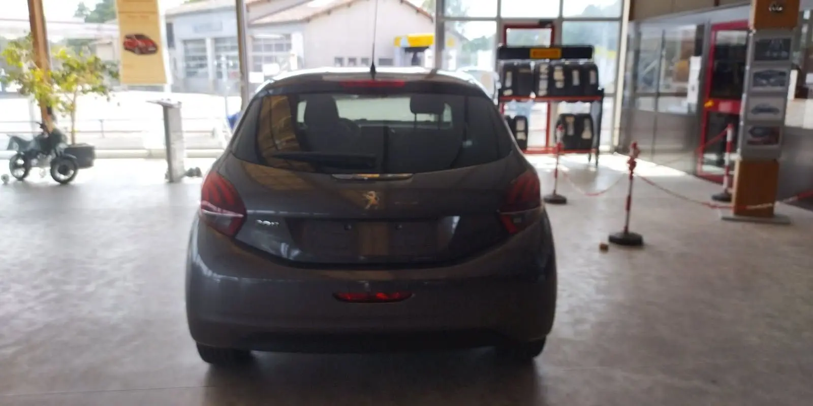 Vue arrière d'une Peugeot 208 gris métal 2023 en showroom, mettant en valeur ses feux arrière et sa silhouette compacte.