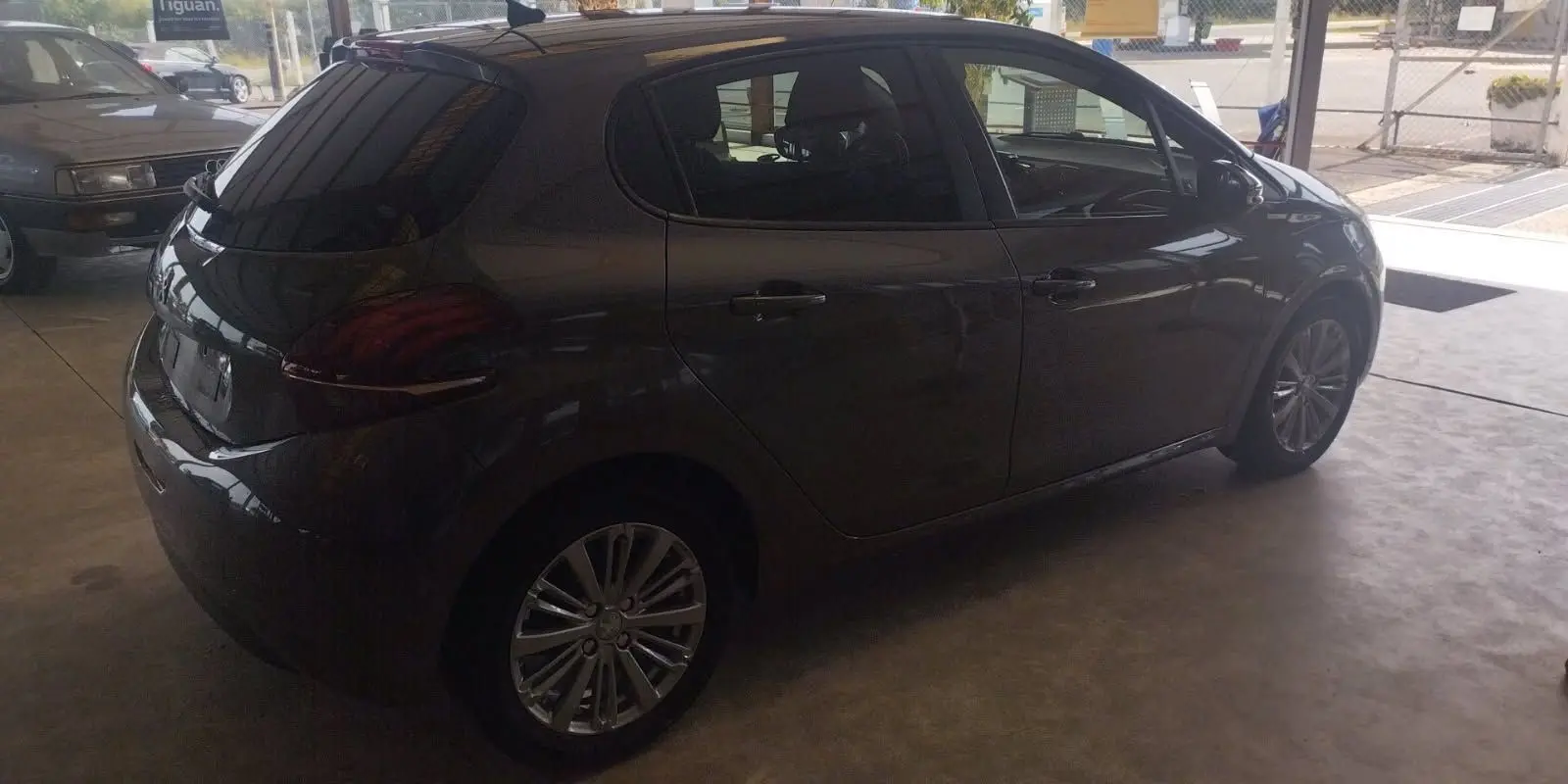 Peugeot 208 gris métal vue de profil côté droit dans un garage, mettant en valeur ses jantes alliage et vitres teintées.