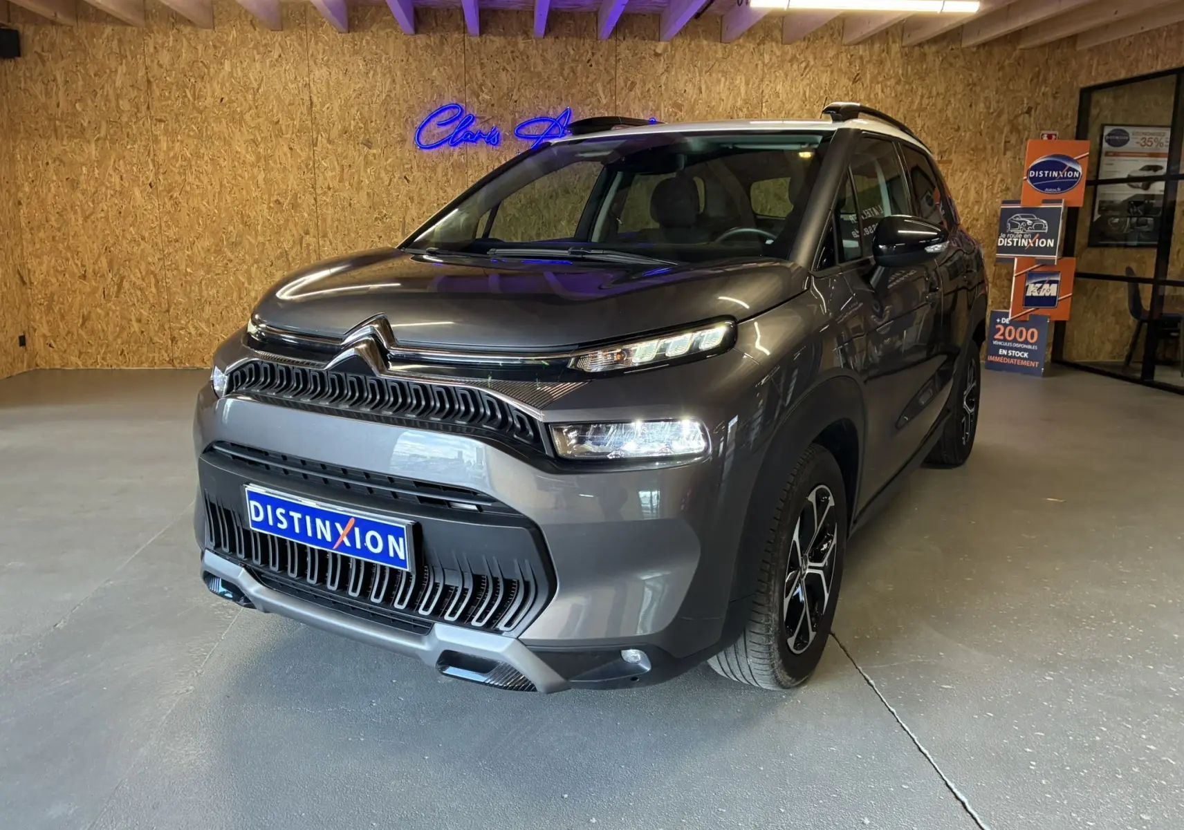 Citroën C3 Aircross gris platinium métal vue 3/4 avant droit avec toit blanc et jantes bi-ton en intérieur showroom.