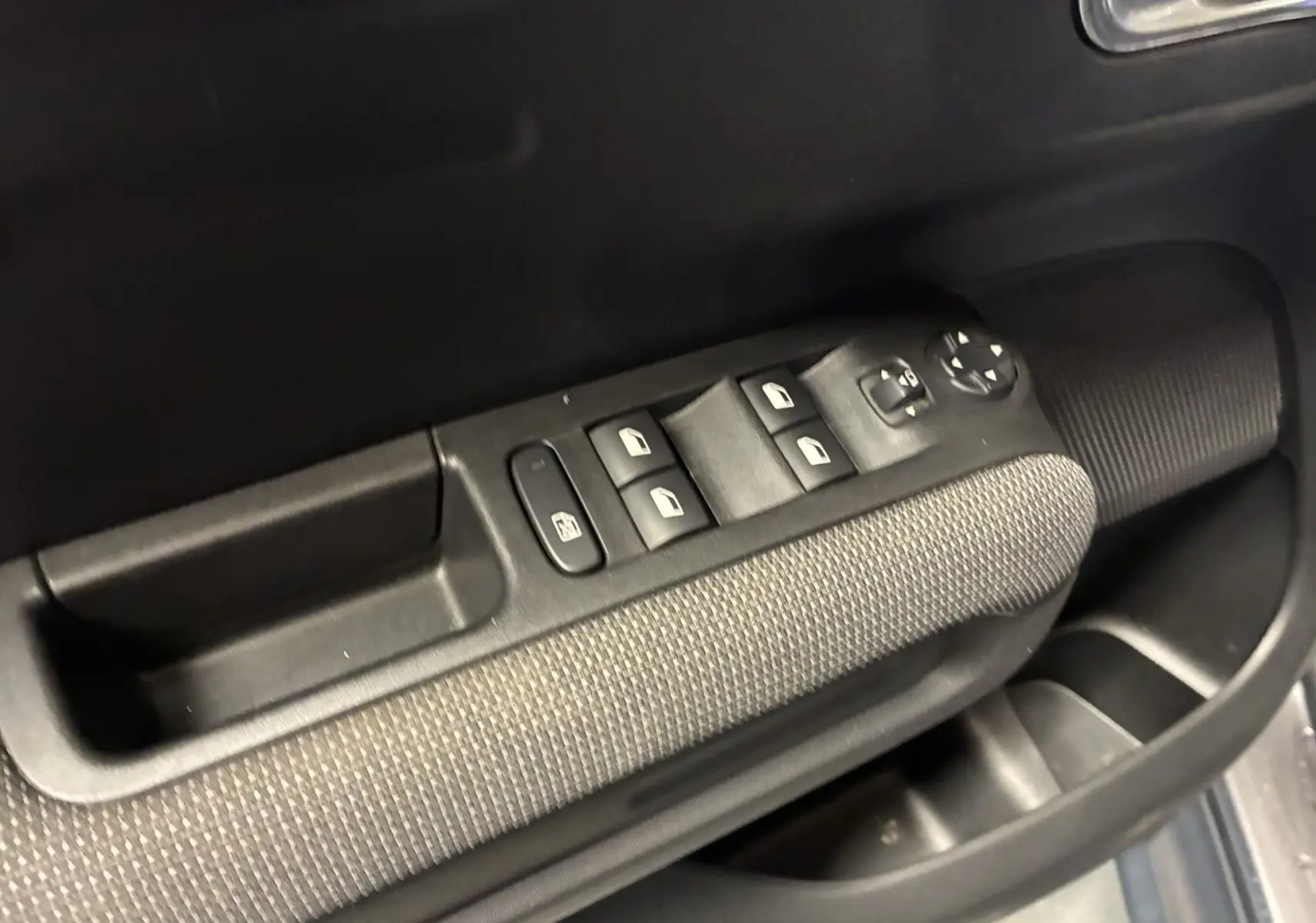 Gros plan sur la commande des vitres électriques côté conducteur avec accoudoir tissu gris noir dans une Citroën C3 Aircross 2023.