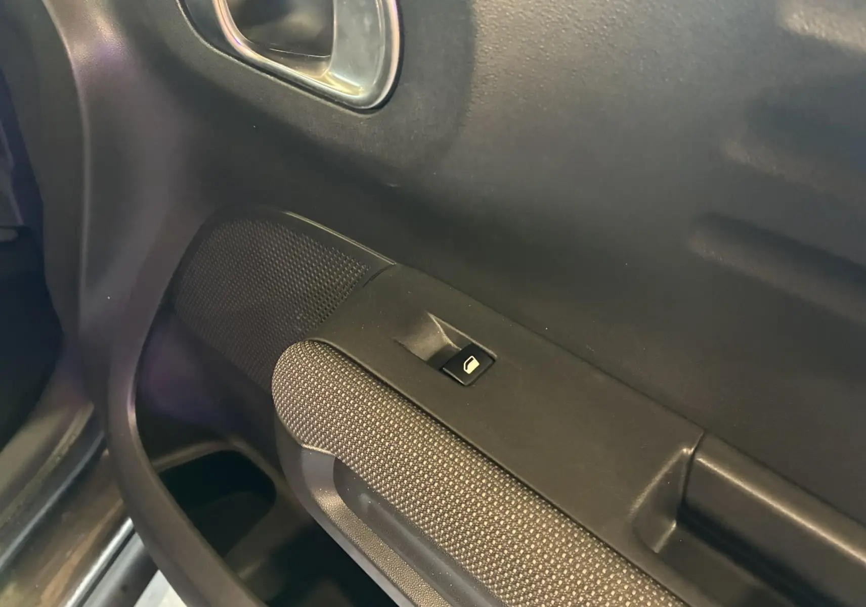 Gros plan sur la commande de lève-vitre côté conducteur avec tissu gris noir et poignée intégrée sur porte Citroën C3 Aircross.