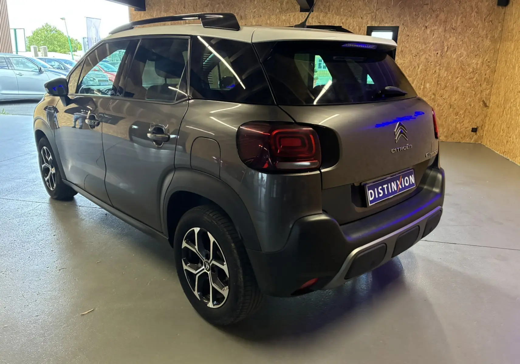 Vue 3/4 arrière droite d'un Citroën C3 Aircross gris platinium métal avec toit blanc et jantes bi-ton en intérieur showroom.