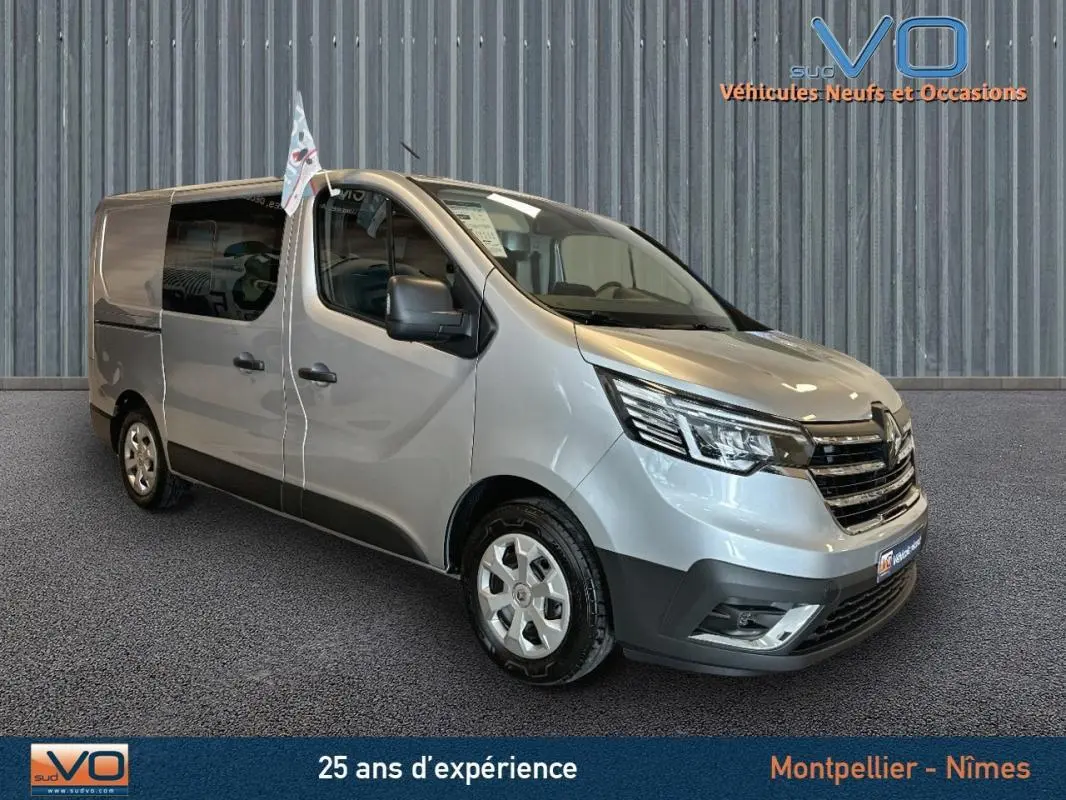 Renault Trafic Fourgon gris en 3/4 avant droit, avec vitres surteintées et calandre noire brillante.