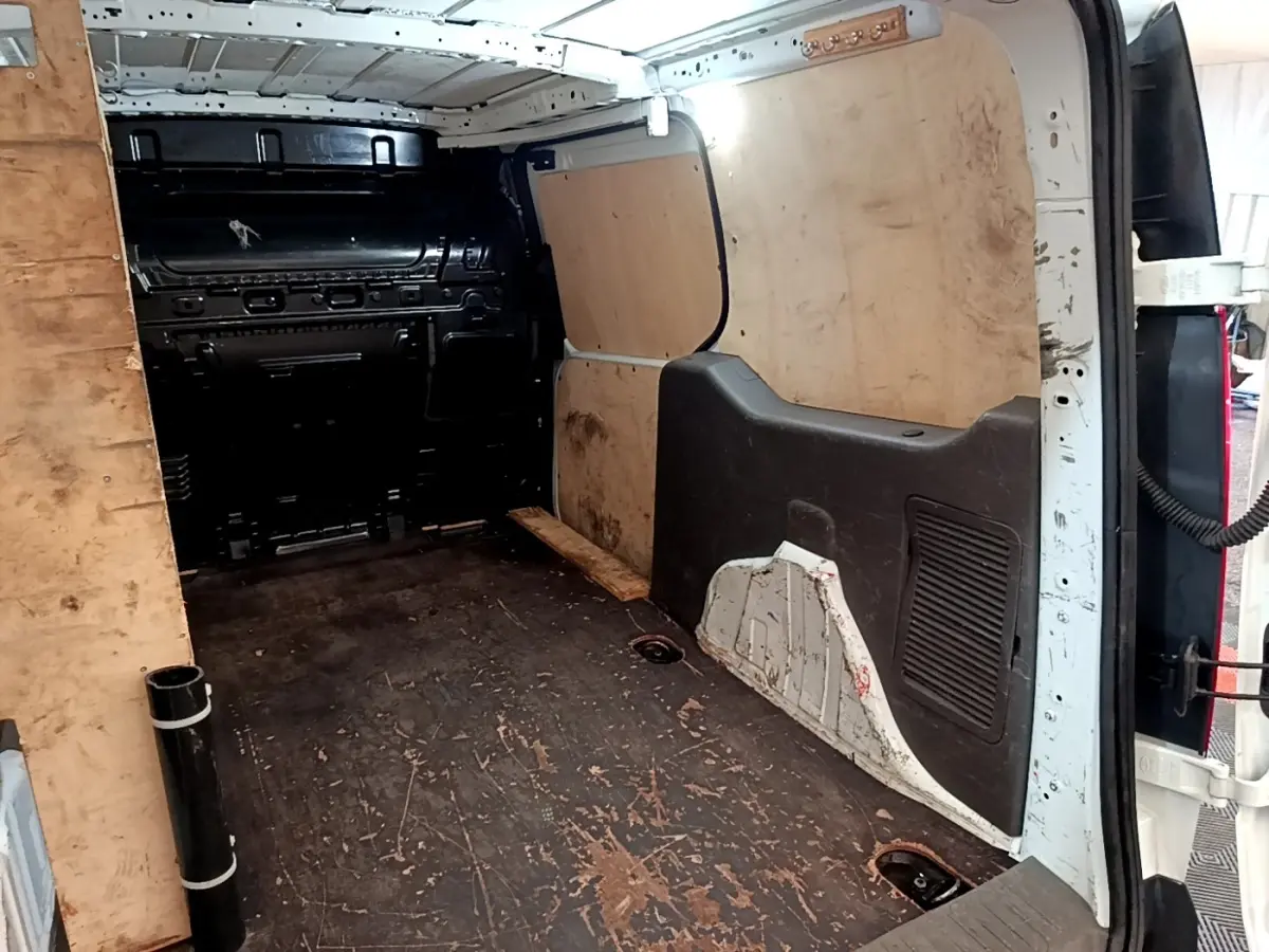Vue intérieure arrière du fourgon Ford Transit blanc, montrant l'espace de chargement avec parois en bois et sol usé.