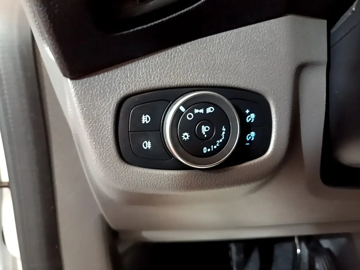 Gros plan sur le bouton de réglage des phares avec éclairage bleu, intérieur gris du Ford Transit Fourgon blanc.