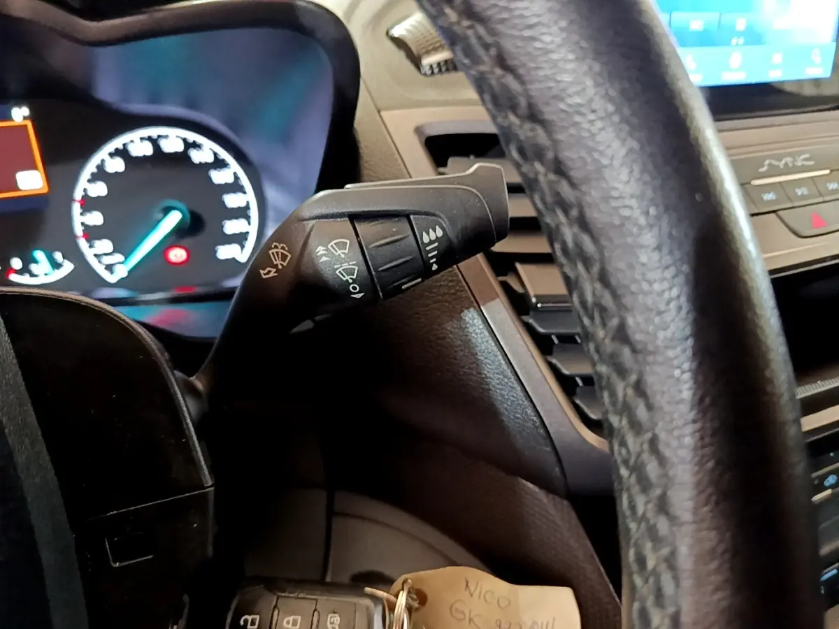 Vue intérieure rapprochée du volant noir et du commodo d’essuie-glace du Ford Transit Fourgon blanc 2022.