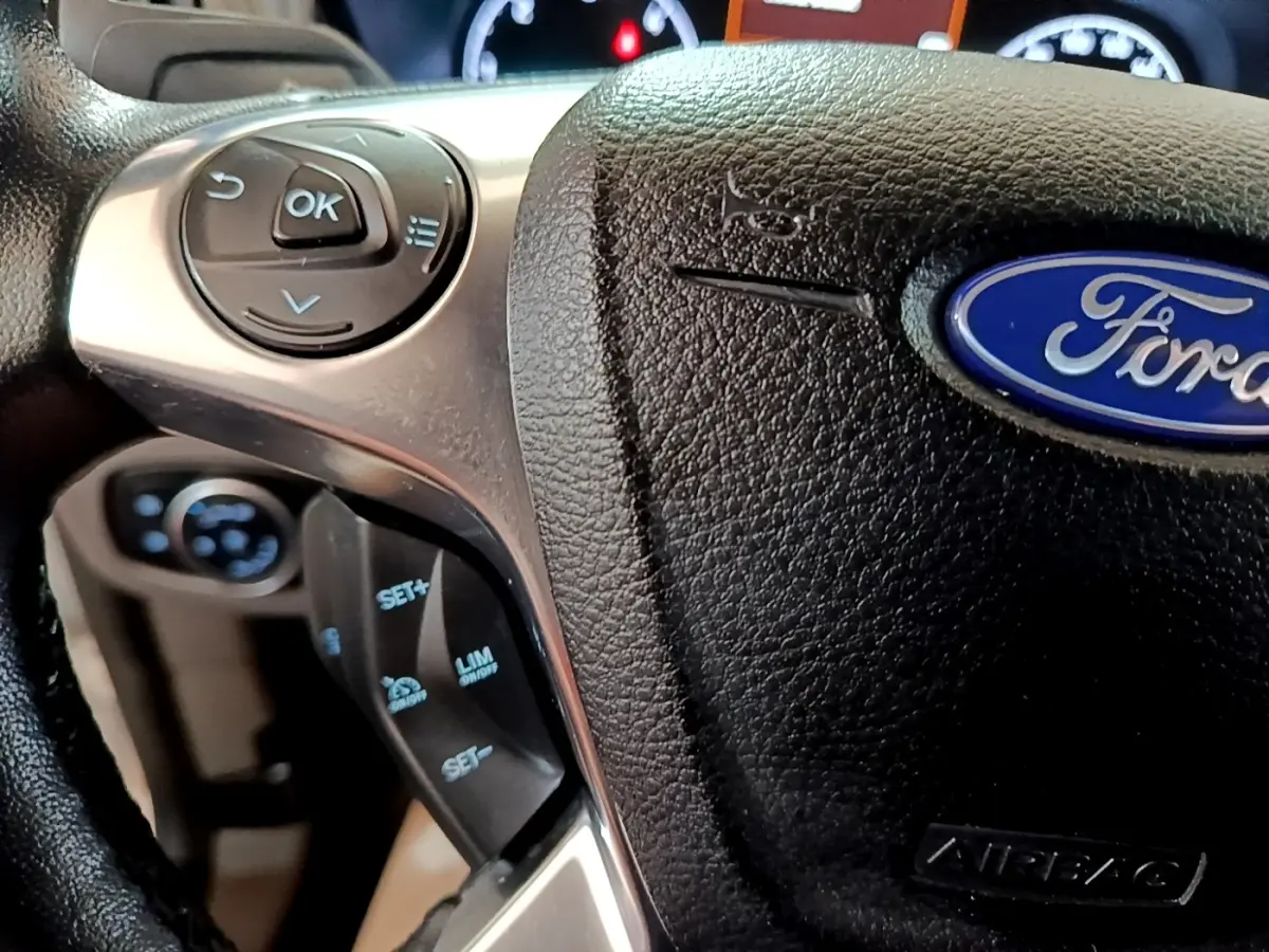 Gros plan sur le volant multifonctions noir du Ford Transit Fourgon blanc, avec commandes de régulateur de vitesse visibles.