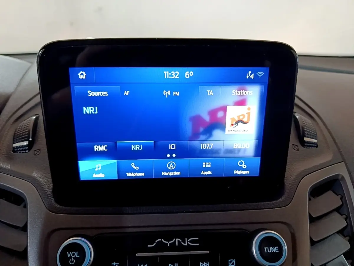 Écran tactile central du tableau de bord du Ford Transit Fourgon blanc, affichant la radio NRJ à 11h32.