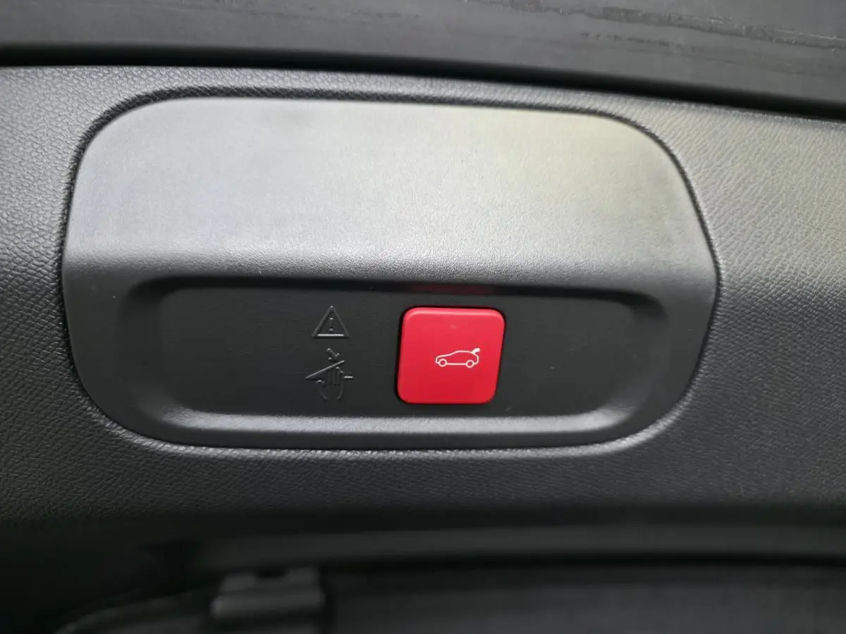 Gros plan sur le bouton rouge d'ouverture motorisée du hayon dans l'intérieur noir du Peugeot 408 gris Selenium.