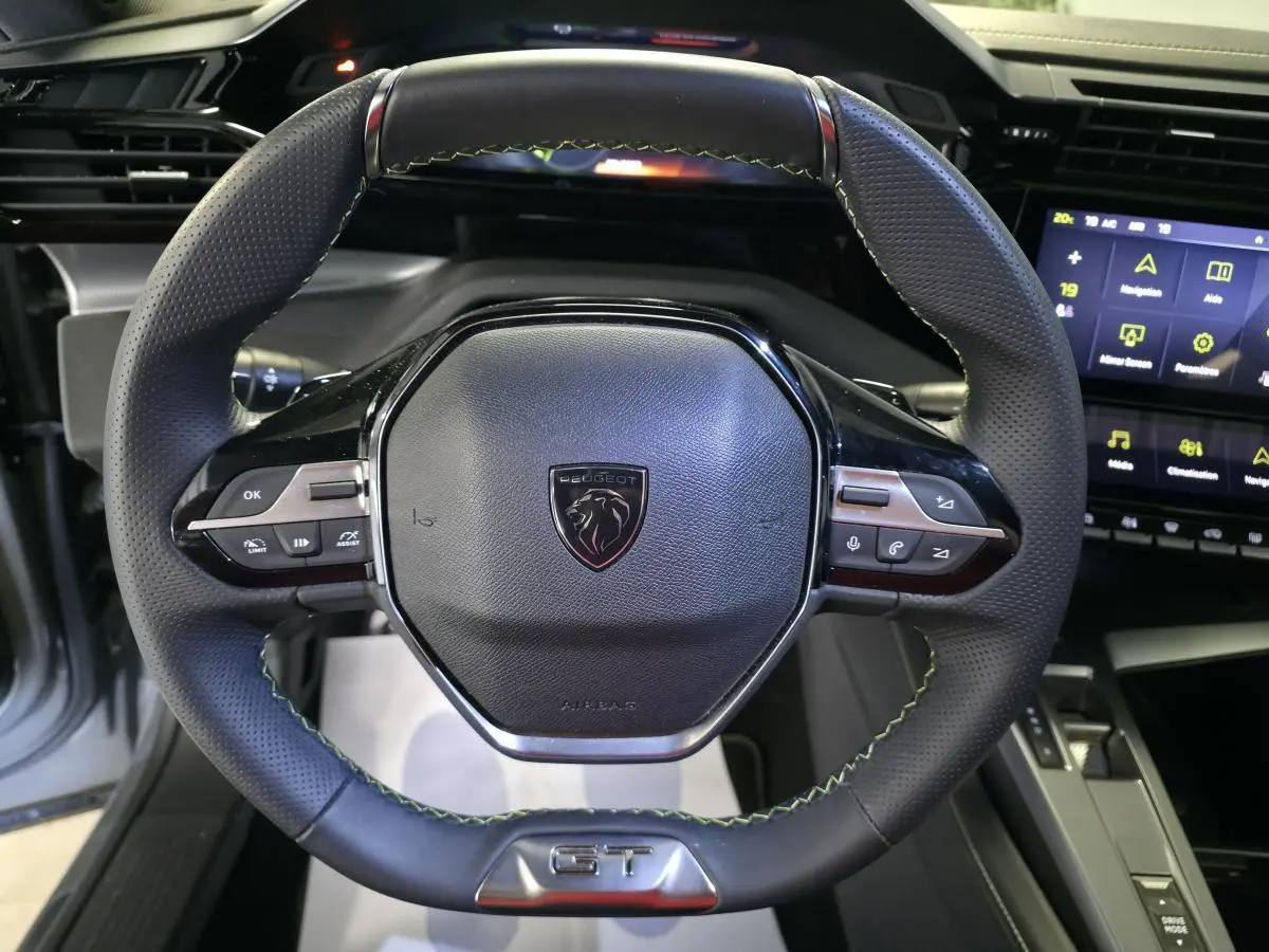 Volant cuir perforé noir avec surpiqûres vertes et logo GT, planche de bord et écran tactile Peugeot 408 hybride rechargeable.