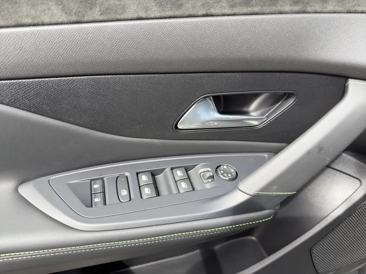 Gros plan sur la porte côté conducteur de la Peugeot 308 gris clair, avec commandes électriques et surpiqûres vertes.