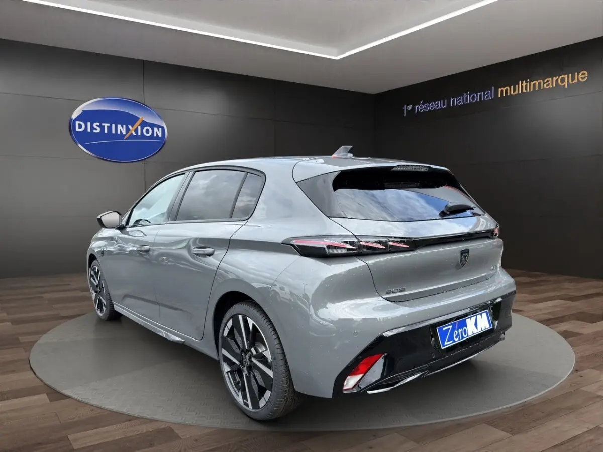 Vue 3/4 arrière droite d'une Peugeot 308 gris clair 2026 avec feux LED et jantes alliage distinctives.