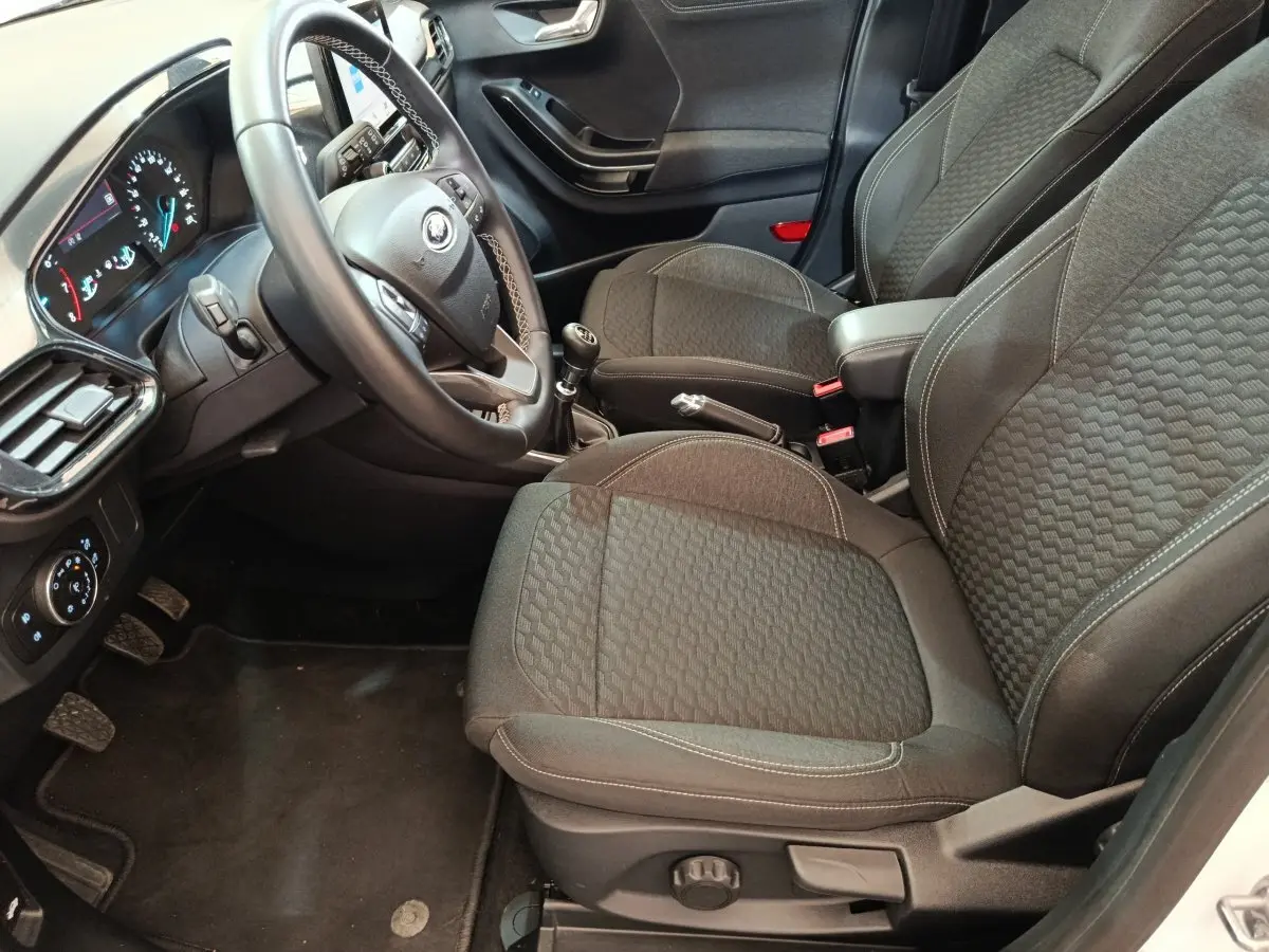 Intérieur avant droit du Ford Puma blanc 2022, sièges tissu gris, volant multifonctions et levier de vitesse manuel visibles.