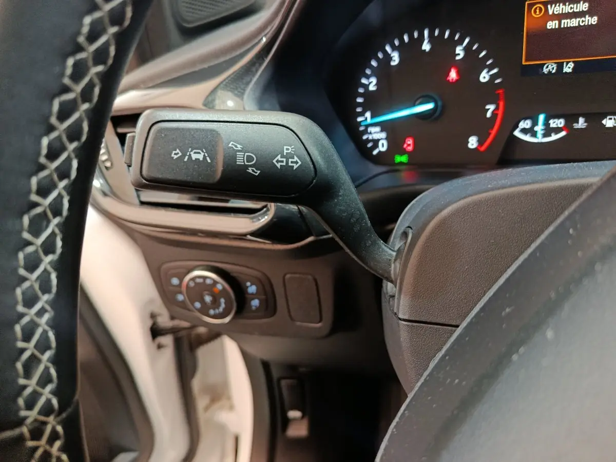 Gros plan sur la commande de clignotants et tableau de bord numérique du Ford Puma blanc, affichage en marche.