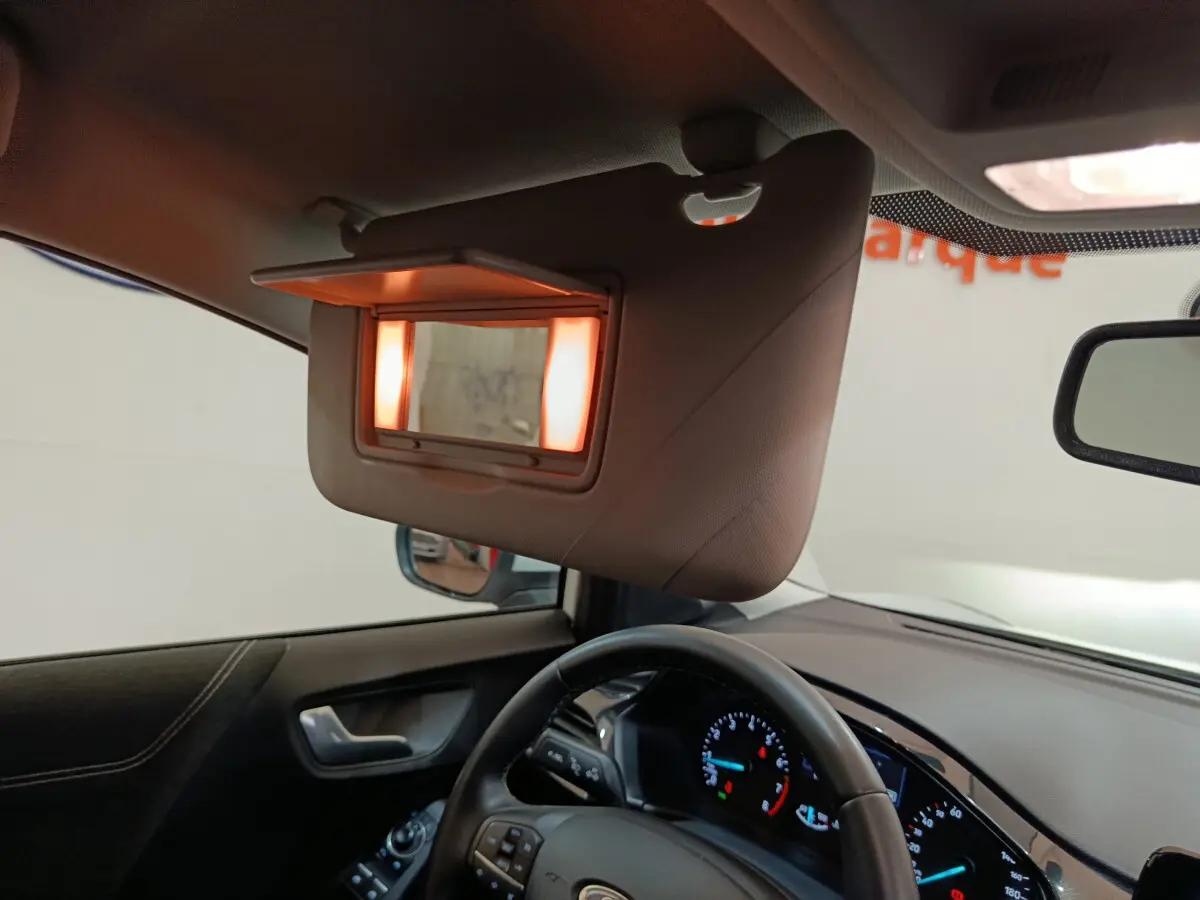 Intérieur du Ford Puma 2022 blanc, vue côté conducteur sur le volant, tableau de bord et miroir de soleil éclairé.