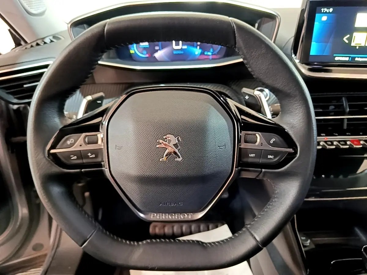 Vue rapprochée du volant cuir noir de la Peugeot 2008 avec commandes intégrées et tableau de bord numérique en arrière-plan.