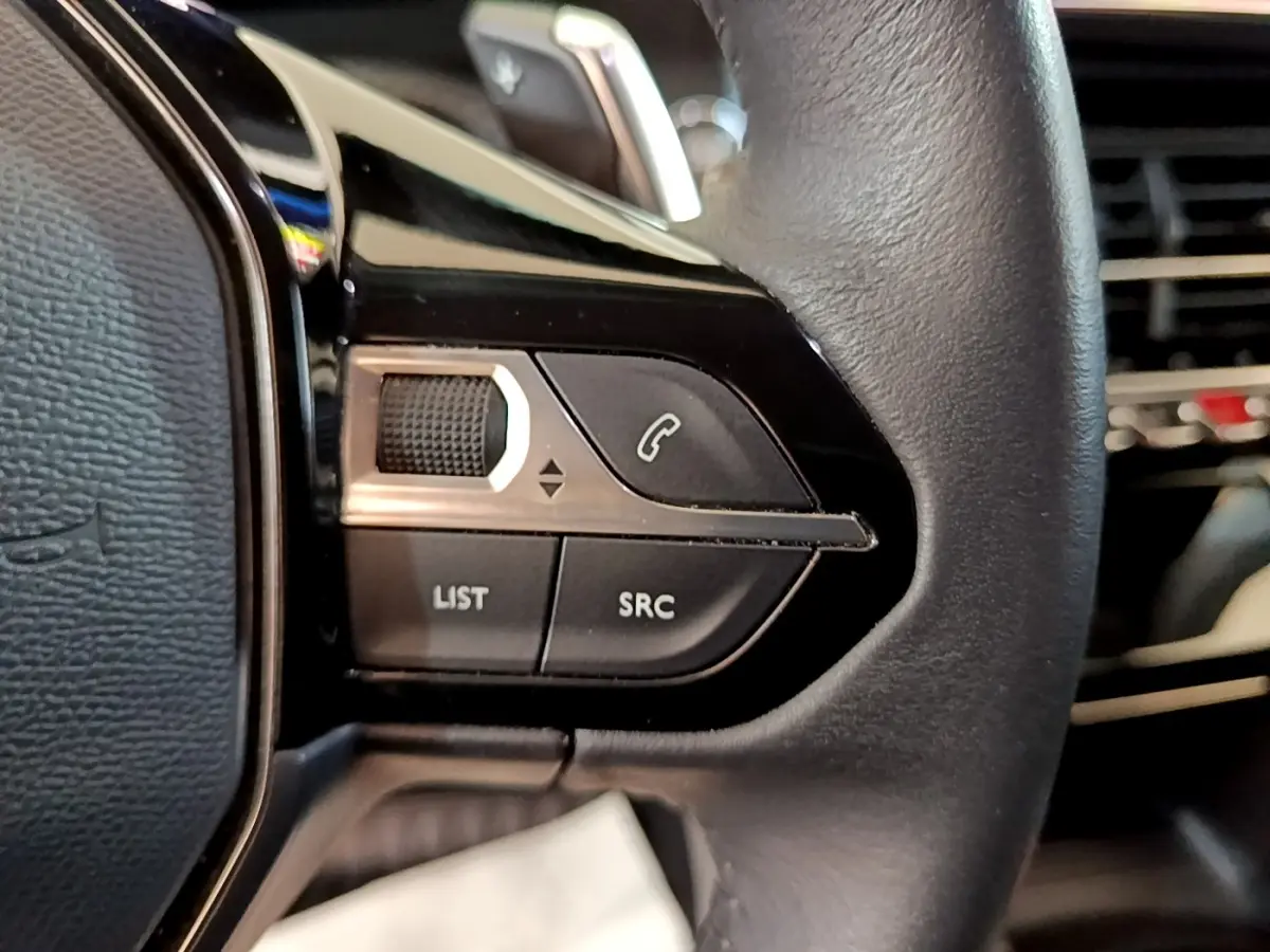 Gros plan sur les commandes gauche du volant cuir noir du Peugeot 2008 gris clair, avec boutons de téléphone et liste.