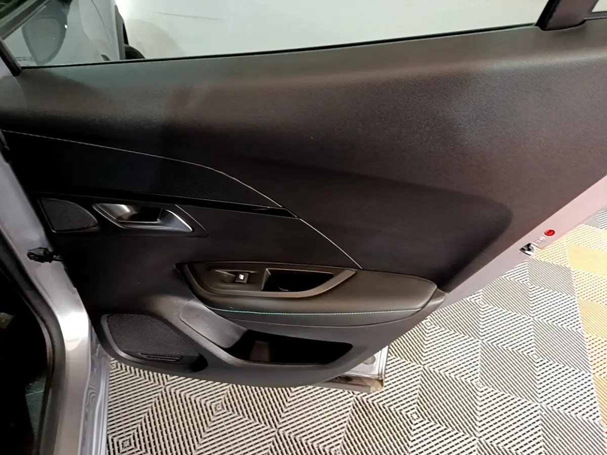 Vue intérieure côté gauche de la porte avant gris clair du Peugeot 2008 avec commandes de vitre et habillage noir.