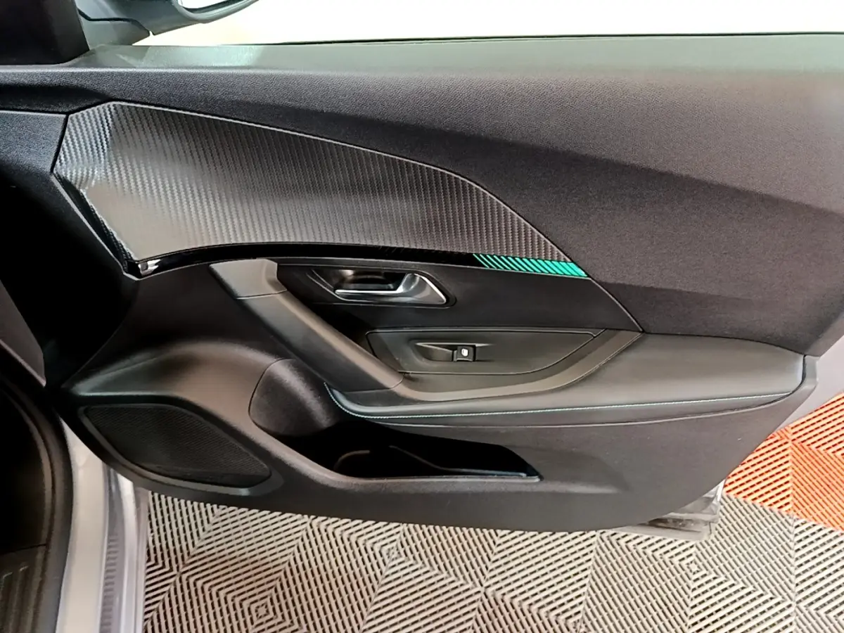 Vue intérieure côté gauche de la porte avant gris clair du Peugeot 2008 avec insert effet carbone et bouton de lève-vitre.