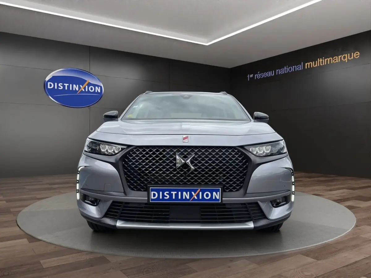 Vue frontale d’un DS7 Crossback gris clair avec calandre noire et feux LED, en showroom Distinxion.