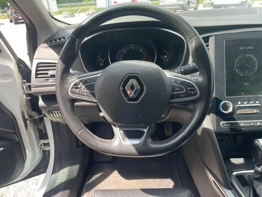 Vue intérieure centrée sur le volant noir de la Renault Mégane IV blanche, avec tableau de bord et écran tactile visibles.