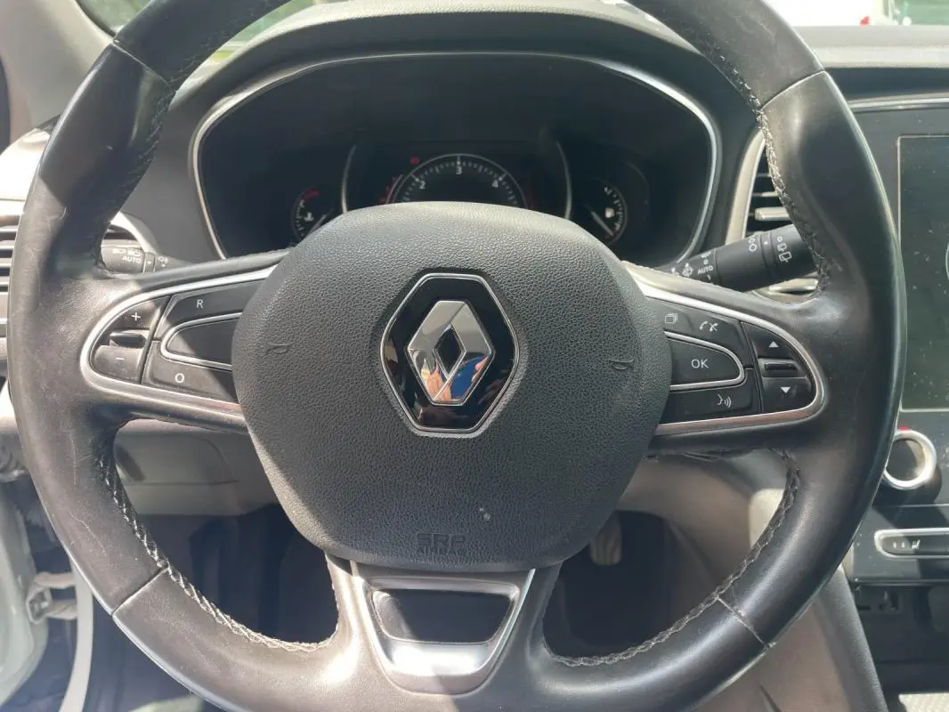 Vue rapprochée du volant noir de la Renault Mégane IV 2016 avec commandes intégrées et logo central chromé.