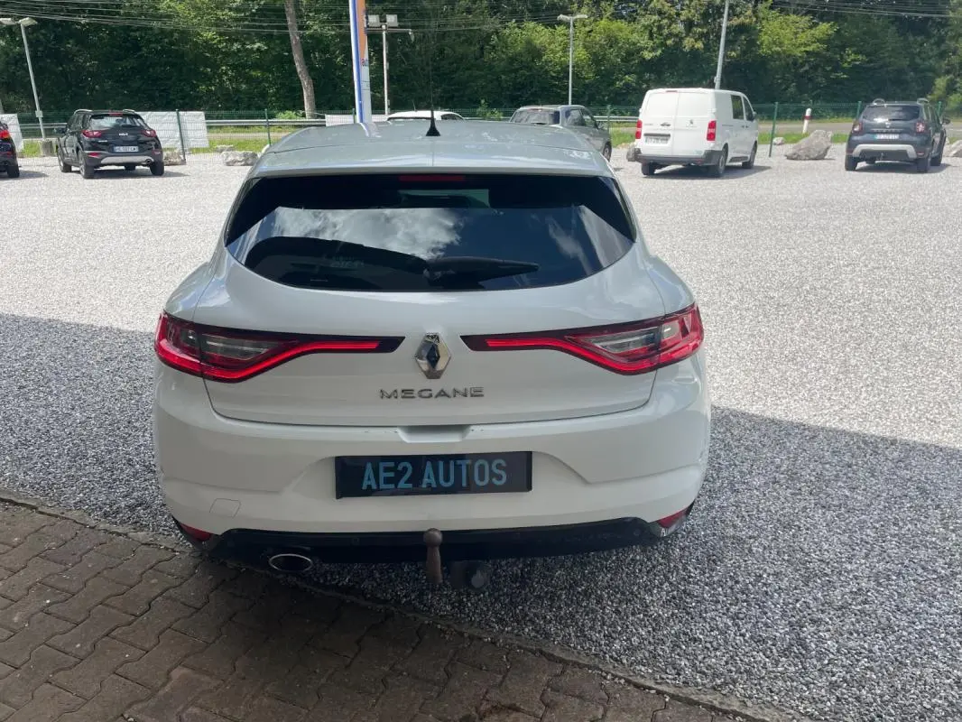 Vue arrière d'une Renault Mégane IV blanche de 2016 avec feux LED allumés et attelage visible.