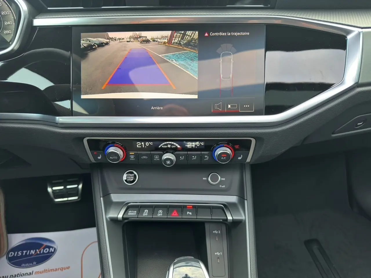 Intérieur de l'Audi Q3 Sportback blanc 2024, vue sur la console centrale avec écran caméra de recul et commandes climatisation.