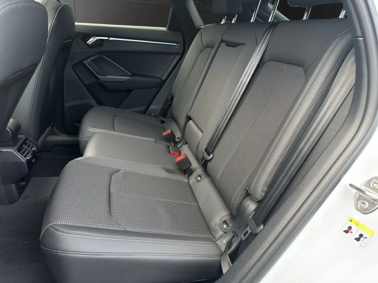 Vue côté droit des sièges arrière noirs en tissu et cuir de l'Audi Q3 Sportback blanc 2024 avec ceintures et porte ouvert.