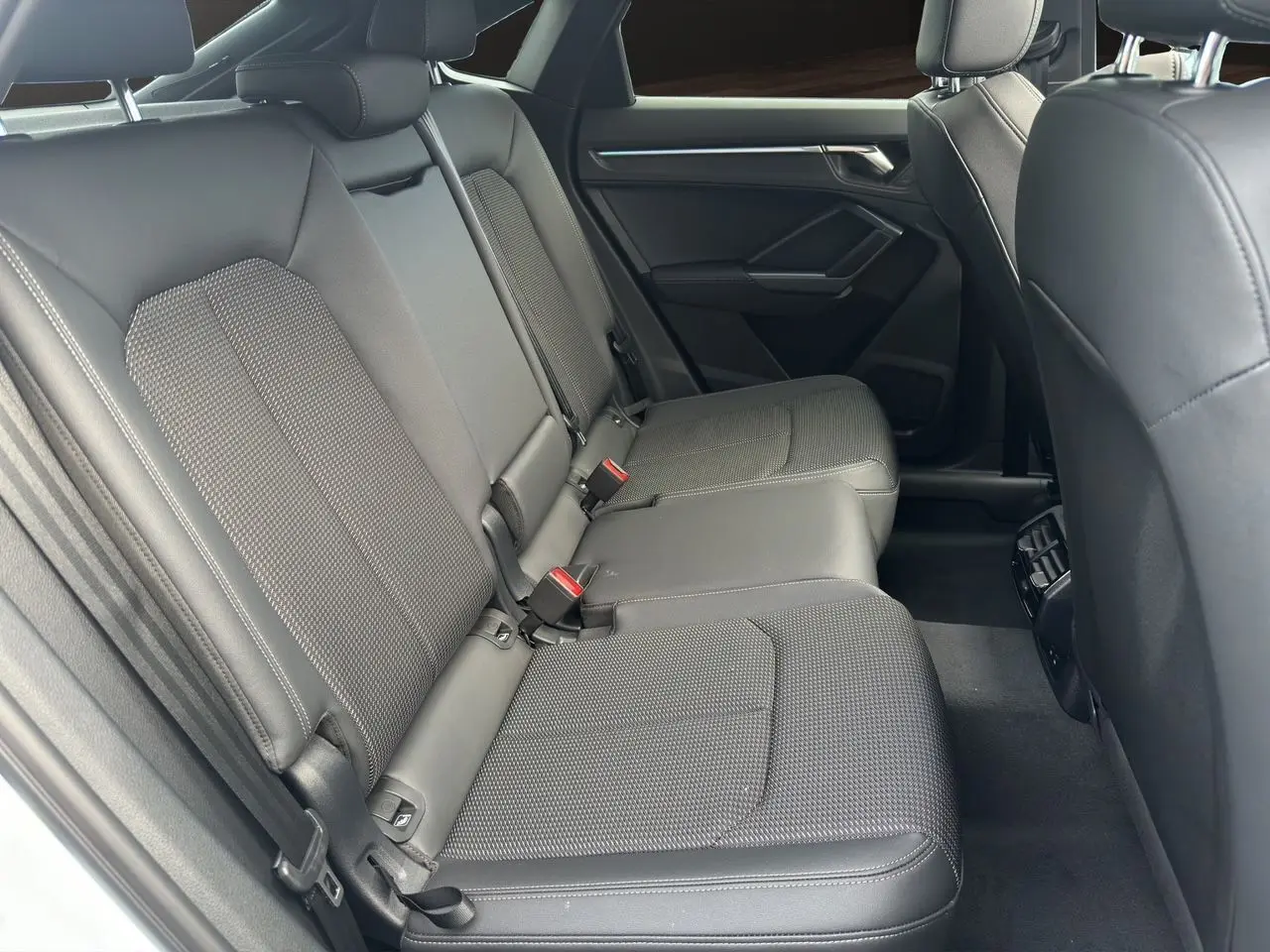 Vue côté droit de la banquette arrière en tissu noir de l'Audi Q3 Sportback S Line 2024 avec ceintures rouges visibles.
