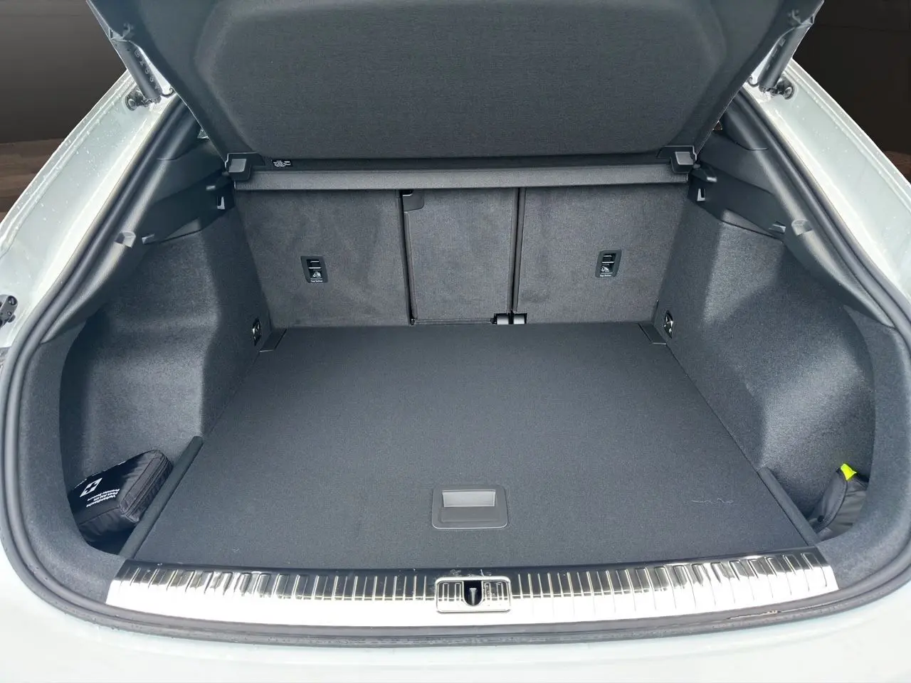 Coffre ouvert d'un Audi Q3 Sportback blanc, montrant un espace de chargement propre et bien fini avec tapis noir.