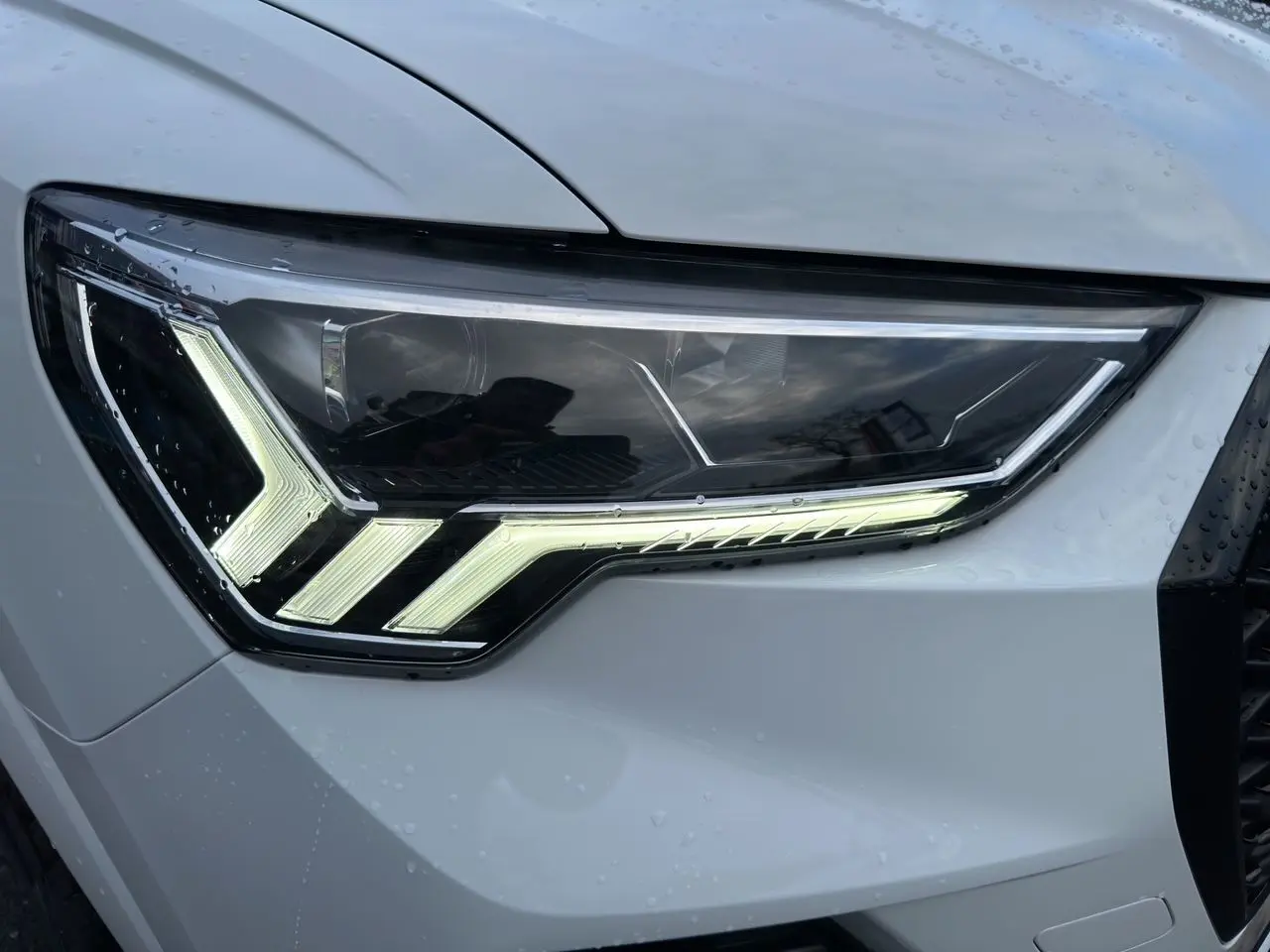 Gros plan sur le phare avant droit LED d'un Audi Q3 Sportback blanc glacier avec éclairage distinctif en forme de flèche.