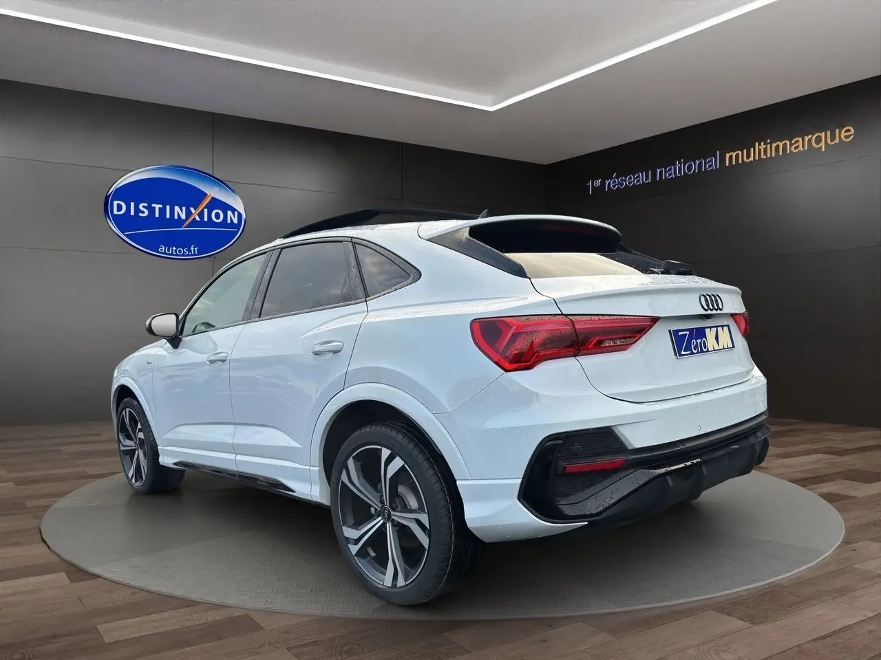 Audi Q3 Sportback blanc vue 3/4 arrière droit, jantes noires brillantes et toit panoramique en showroom.